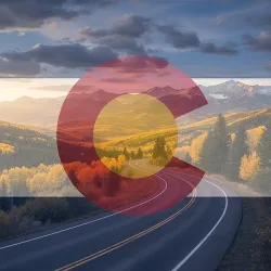 An image showing a winding road through Colorado mountains with golden autumn foliage, under a partly cloudy sky at sunset. A transparent overlay of the Colorado state flag (red C, gold circle, and white and blue stripes) is visible over the landscape.